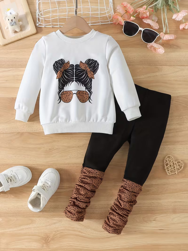 Children's outfit with white sweatshirt and black leggings on a wooden surface.